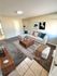 Inviting living room with plush carpet, stylish sectional sofa, contemporary artwork, and modern wooden furniture.