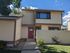 Charming two-story home with a welcoming red door, surrounded by lush greenery and a neat pathway.