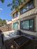 Charming backyard view of a townhouse featuring a sunlit patio, modern air conditioning unit, and a small garden bed, perfect for outdoor relaxation.