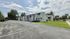 Charming white apartment complex with lush greenery and ample parking under a bright, blue sky.