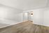 Bright and spacious open-plan living area with sleek laminate wood flooring and crisp white walls, leading to a cozy kitchen nook with modern appliances.