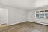 Bright and airy living space with sleek wood flooring, large window for natural light, and access to a cozy room.
