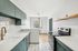 Modern kitchen with sleek white countertops, stylish green cabinetry, and stainless steel appliances, featuring elegant subway tile backsplash and natural light from the large window.