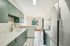 Modern apartment kitchen with sleek green cabinets, marble countertops, and stainless steel appliances, featuring a large window for natural light.