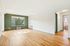 Bright and airy living room with hardwood floors, large window offering lush views, and fresh white and green walls.