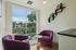 Cozy nook with plush purple chairs and a modern bookshelf, bathed in natural light from a large window overlooking lush greenery.