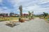 Vibrant urban park setting with modern apartments in the background, featuring well-maintained pathways, picnic tables, and lush greenery under a clear blue sky.