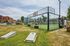 Vibrant outdoor padel court with clear glass walls in a lively urban setting, surrounded by modern buildings and green space.