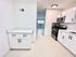 Bright, modern kitchen with sleek white cabinets, stainless steel appliances, and elegant countertops flowing into a spacious open living area.