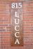 Elegant wooden sign with white letters displaying '815 LUCCA,' set against a classic red brick wall.