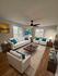 Inviting living room with modern decor, white sofas accented by teal cushions, stylish artwork, and wooden furniture for a cozy ambiance.