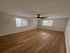 Bright and airy room with sleek wood flooring, featuring large windows and a modern ceiling fan.
