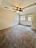 Bright and inviting room with plush carpet, ceiling fan, and ample natural light from large windows and glass door.