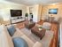 Bright and modern living room with stylish decor, featuring a large wall-mounted TV, cozy beige sofa, and elegant wood flooring.