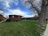 Charming brick apartment building nestled in a lush green yard with mature trees and a vibrant blue sky backdrop.