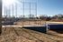 Charming baseball field under clear blue sky, featuring well-maintained diamond and backstop, surrounded by lush greenery and trees.