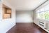 Bright living area with elegant wood flooring and large window offering garden views, adjacent to a cozy kitchen space.