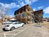 Charming three-story apartment building with spacious balconies, ample parking, and a bright blue sky backdrop.