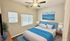 Inviting bedroom with a large bed featuring blue accents, modern decor, natural light from two windows, and a serene mountain landscape art piece.