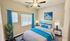 Inviting bedroom with elegant decor, featuring a plush bed adorned with vibrant blue accents, modern artwork, and abundant natural light through wide windows.