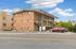 Charming three-story brick apartment building with convenient outdoor staircases and ample parking, set against a bright blue sky.