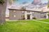 Charming two-story apartment building with a welcoming entrance set against a picturesque sky, surrounded by lush green lawn and mature trees.