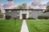 Charming apartment building with modern gray facade amidst lush greenery and a vibrant lawn, set against a picturesque sky.