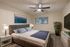 Inviting bedroom with plush bedding, stylish decor, and natural light from a large window; features sleek furnishings and a calming plant for a serene atmosphere.
