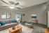 Inviting living room with modern gray sofa, vibrant teal cushions, and stylish wicker chair, enhanced by chic decor and natural light from large windows.