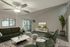 Modern living room with elegant dark green sofa set, stylish rug, sleek ceiling fan, and large TV unit, featuring a spacious balcony view and lush potted plant accent.