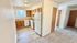 Bright and cozy apartment kitchen with light wood cabinets and modern appliances, seamlessly connecting to a soft carpeted hallway.