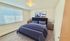 Bright and cozy bedroom featuring a plush bed with navy bedding, elegant side tables, and captivating modern artwork, enhanced by natural light from large windows.