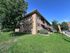 Charming brick apartment building surrounded by lush greenery and clear skies, offering a serene residential environment.