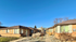 Charming brick duplex units with large windows and a sunny walkway, surrounded by a clear blue sky and peaceful landscaping.