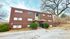 Charming three-story brick apartment building with lush greenery and modern entryway, nestled in a serene suburban setting.