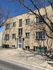 Charming brick apartment building with classic architectural details, framed by tree shadows on a sunny day.
