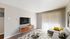 Contemporary living room with a sleek wall-mounted TV, stylish wooden cabinet, and bright natural light from tall vertical blinds.