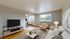 Bright open-plan living room with cozy seating, modern TV setup, and dining area, enhanced by large windows and stylish d&eacute;cor.