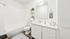 Virtually staged modern bathroom showcasing a pristine white bathtub, sleek vanity with ample counter space, and elegant shelving for toiletries. Warm wood flooring adds a touch of sophistication.