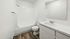 Modern bathroom with sleek white fixtures, a spacious bathtub, elegant vanity, and beautiful wood-patterned flooring.