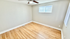 Bright, spacious room with polished hardwood floors and natural light from a wide window, perfect for a cozy bedroom or home office.