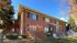 Charming red-brick apartment building with elegant windows and a beautifully landscaped entrance, set against a clear blue sky.