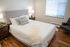 Cozy and stylish bedroom with a plush bed, elegant wood floors, and ample natural light creating a serene atmosphere.