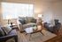 Bright and inviting living room featuring cozy gray seating, stylish wood accents, and abundant natural light from large windows.