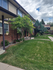Charming apartment exterior with lush green lawn, vibrant flowers, and inviting walkway under a bright, cloudy sky.