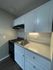 Modern kitchenette with sleek white cabinets, a compact stove, and granite countertops.