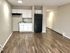Sleek kitchen with white cabinetry, black refrigerator, and wood laminate flooring in a modern apartment.