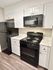 Contemporary kitchen featuring sleek black appliances, white cabinets, and marble countertops.