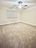 Spacious bedroom with soft carpet, ceiling fan, and natural light from window.