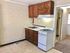 Compact kitchen featuring wooden cabinetry, gas stove, and sink area with light brick wall.